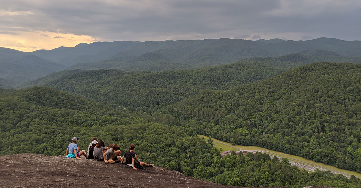 teenage boys and girls sitting on a rock face in front of a mountain view