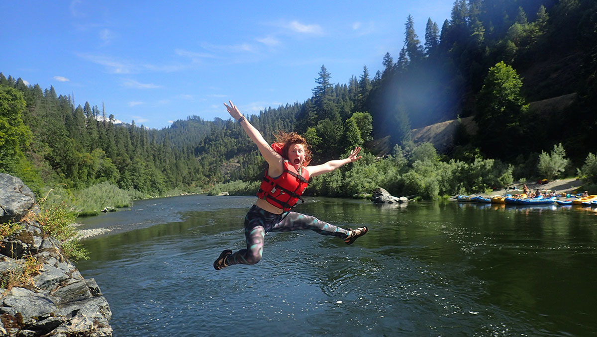 teenage girl in red life vest jumping off rock into river