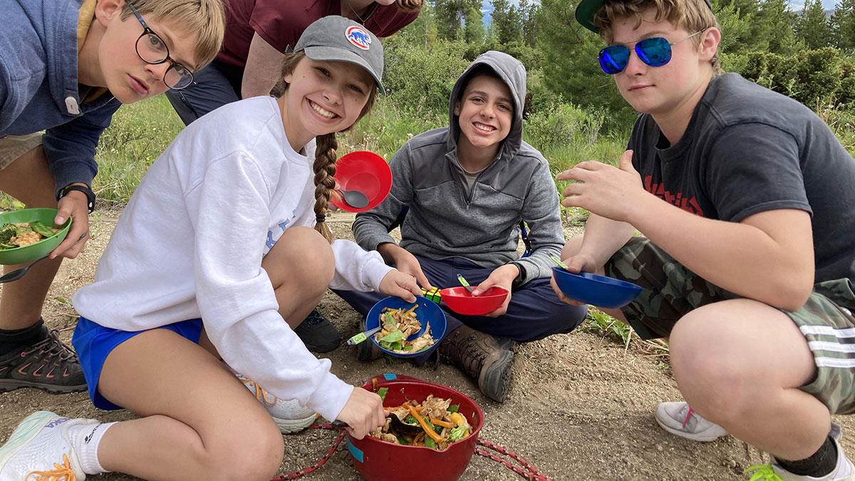 teenagers cooking meals outside while camping